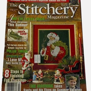 May include: The Stitchery Magazine, July 1996, features a cross-stitch Santa Claus on the cover. Additional text includes "Stitch Christmas This Summer" and "8 Steps to Finishing Fab Stockings." Decorative Santa figurines and a sleigh are also visible.