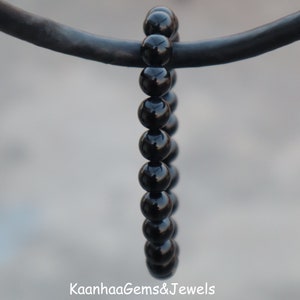 Peut inclure: Un bracelet noir en perles avec une finition brillante. Le bracelet est composé de perles rondes et est enfilé sur un cordon noir.