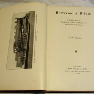 May include: A vintage book titled "Betterment Briefs: A Collection of Published Papers on Organized Industrial Efficiency" by H.W. Jacobs. The book cover is cream colored with black text. The book was published in 1909 by John Wiley & Sons in New York.