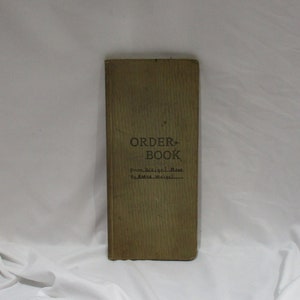 May include: A vintage green order book with the text "ORDER BOOK" in black lettering. The book has the text "From: Weigel Bros. To: Anna Weigel" written in black ink.