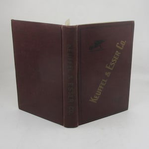 May include: An open, maroon-colored book with gold lettering and a logo on the cover. The spine and cover read "Keuffel & Esser Co.". The book is set against a plain white background.