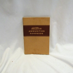 May include: A tan-colored book with a maroon stripe and the text "Western Ammunition Handbook" printed on the front cover.