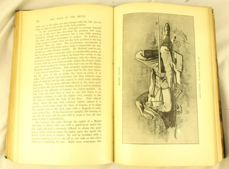 May include: An open book with text and a black and white illustration of a person holding a rifle. The illustration is on the right page, and the text is on the left page. The book has aged yellow pages.