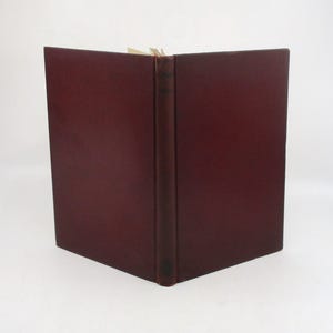 May include: A dark red leather-bound book with a spine that is slightly raised. The book is closed and lying flat on a white surface.