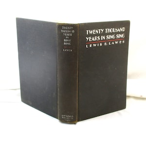 May include: A hardcover book titled "Twenty Thousand Years in Sing Sing" by Lewis E. Lawes. The book has a black cover with white text and a red underline. The spine is dark brown with white text. The book is open, displaying the title.