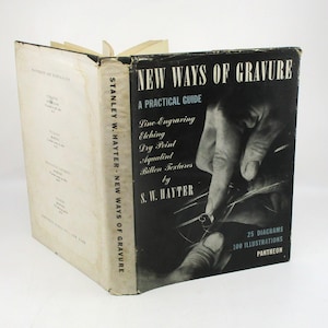 May include: An open book titled "New Ways of Gravure" by S.W. Hayter. The cover is black and white, featuring a hand engraving. The book's spine reads "Stanley W. Hayter New Ways of Gravure". The book is a practical guide to printmaking.