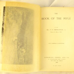 May include: An open book titled "THE BOOK OF THE RIFLE" with aged, yellowed pages. The left page features a black and white illustration. Published in 1901 by Longmans, Green, and Co. The text includes the author's name, H. T. F. Fremantle.