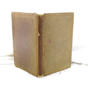 May include: An antique book with a worn, brown cover and spine. The book is open, revealing the aged pages. The spine has the title printed on it. The cover has a faded, reddish-brown hue.