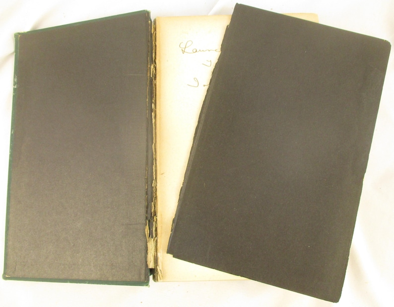 May include: An open antique book with a dark green cover on the left and a black cover on the right. The pages are off-white with handwritten script. The book's spine is visible, showing the binding.
