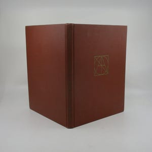 May include: A brown hardback book with a gold geometric design on the cover. The design features a stylized letter "A" within a square.