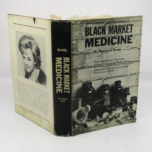 May include: A hardcover book titled "Black Market Medicine" by Margaret Kreig. The cover features a black and white photo of a woman and a brick wall background. The book's spine is black with white text.