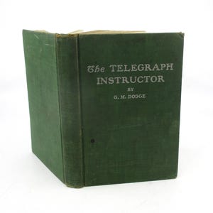 May include: A vintage green book titled "The Telegraph Instructor" by G. M. Dodge. The book's cover is a dark green color with the title and author's name in a lighter font. The book appears to be in good condition.