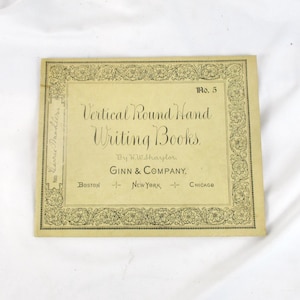 May include: A vintage book cover with the title "Vertical Round Hand Writing Books" by W.W. Shaylor. The cover is a light tan color with decorative floral borders and the publisher's name, Ginn & Company, and city locations.