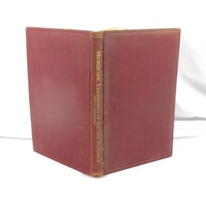 May include: An open, antique book with a maroon cover and spine. The spine displays the title "Microscopic Examination of the Ore Minerals" and the author's name. The book is set against a white background.