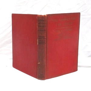 May include: A red hardcover book titled The Riddle of the Rhine by Victor Lefebure. The front cover and spine feature embossed text. The book is standing upright, showing the front cover and the spine, with a worn texture on the red fabric cover.