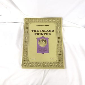May include: A vintage copy of "The Inland Printer" magazine from February 1928. The cover is a light tan color with ornate gold borders and text. The magazine's title is prominently displayed, along with a small illustration and the volume and issue numbers.