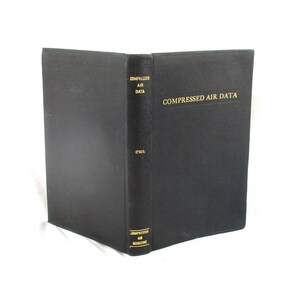 May include: A black hardcover book titled "Compressed Air Data" with gold lettering. The book is open, revealing the spine and the front cover. The spine also has text, and the book is on a white background.