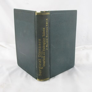 May include: A vintage book titled "Surgical Diseases of the Ovaries and Fallopian Tubes" by J. Bland Sutton F.R.C.S. The book has a dark green cover and spine with gold lettering. The book is open, displaying the spine.