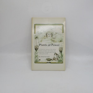 May include: Book cover with a green, yellow, and brown illustration of a Native American person with feathers and animals. The title of the book is "Plants of Power: A historical survey of the divine nature of plants and ritual communication through plant helpers to the spirit world." by Alfred Savinelli.