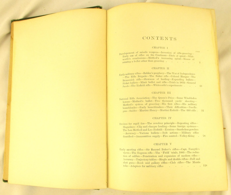 May include: An open book with aged, yellowed pages, revealing the contents page. The text details chapters and subheadings on rifles and related subjects. The book is open at a double-page spread.