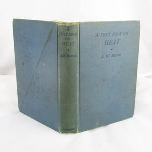 May include: A vintage textbook titled "A Text Book on Heat" by A.W. Barton. The book has a blue cover and a green spine. The text is printed in a simple, sans-serif font. The book is slightly worn, suggesting age.