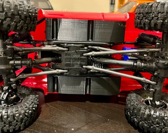 May include: A red toy truck with black tires and a detailed undercarriage, showing the suspension and axles. The truck is on a brown surface.