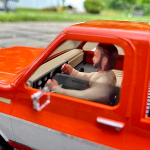 May include: A bright orange toy truck with a white stripe and a black roll bar. The truck has a driver in the cab and a bed in the back. The truck has a "K5 BLAZER" sticker on the side.