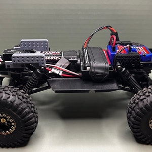 May include: A black and gray radio-controlled car chassis with a black and gray battery pack, a black and red servo, and a black and white motor. The car has black wheels with gold rims and a black and gray body.