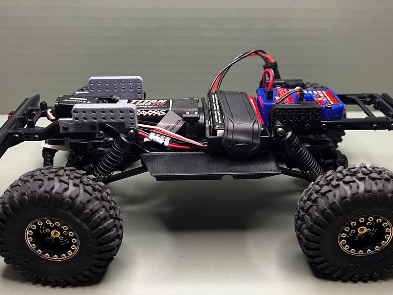 May include: A black and gray radio-controlled car chassis with a black and gray battery pack, a black and red servo, and a black and white motor. The car has black wheels with gold rims and a black and gray body.