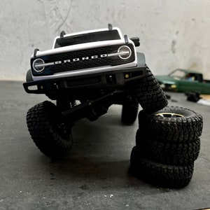 May include: A white Ford Bronco model car with black tires. The car is on its side and the tires are stacked on top of each other.