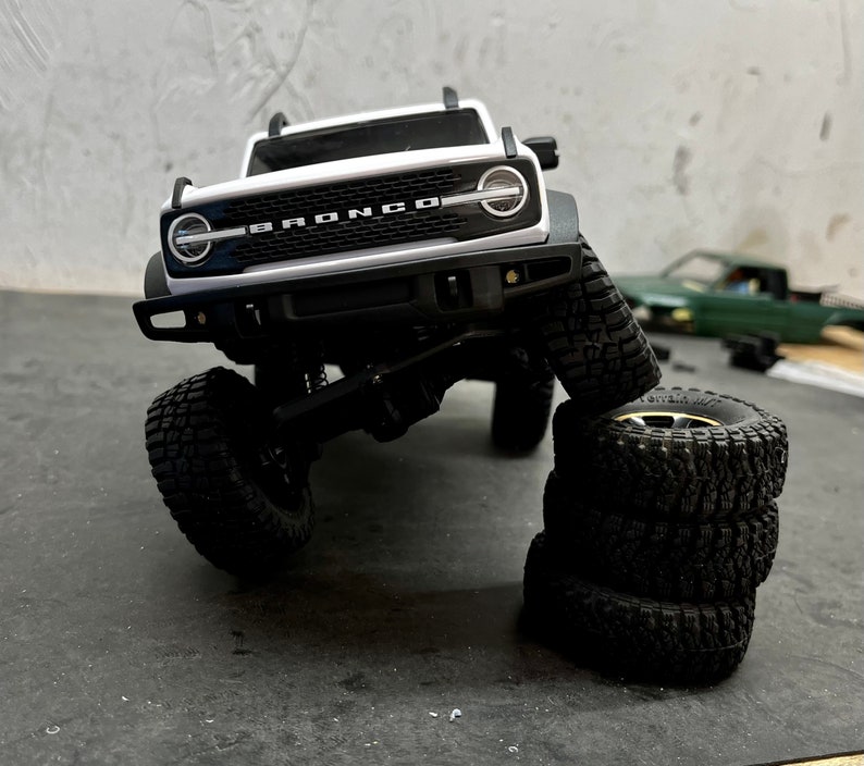 May include: A white Ford Bronco model car with black tires. The car is on its side and the tires are stacked on top of each other.