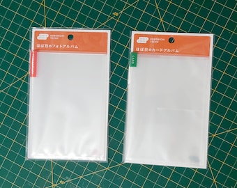 Puede incluir: Dos álbumes de fotos de plástico transparente con embalaje naranja y blanco. El álbum de la izquierda está etiquetado como "ほぼ日のフォトアルバム" y el álbum de la derecha está etiquetado como "ほぼ日のカードアルバム".
