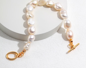 Peut inclure: Un bracelet en perles blanches avec un fermoir et une glissière dorés. Les perles sont de forme irrégulière et ont un lustre naturel.