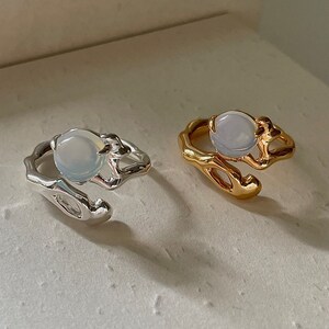 May include: Two rings with a white stone set in a gold and silver abstract design.