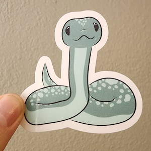 May include: A sticker of a light blue snake with white spots. The snake has a cute cartoon face with big eyes and a small mouth.