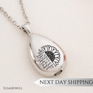 May include: A silver-toned teardrop pendant necklace featuring an engraved sunflower and the text: He who began a good work in you will carry it on to completion until the day of Christ Jesus Philippians 1:6. The pendant hangs from a silver chain.