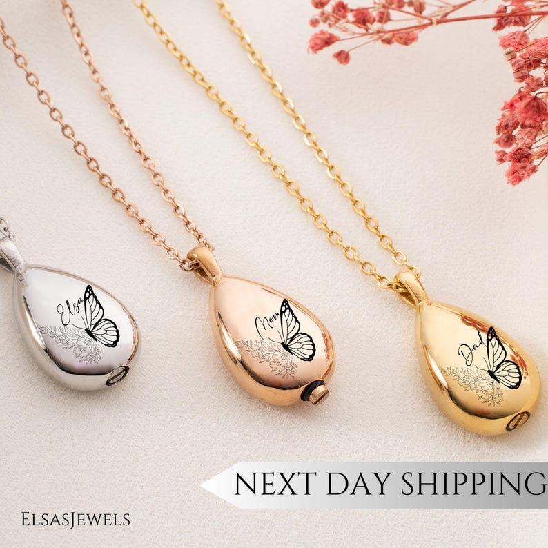 Op de afbeelding: Drie traanvormige gedenkkettingen in zilver, ros&eacute;goud en goud. Elke hanger heeft een vlinderontwerp en gepersonaliseerde tekst. De kettingen hangen aan delicate kettingen. De tekst "Next Day Shipping" is zichtbaar.
