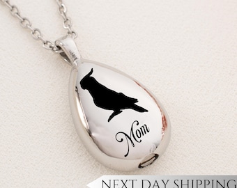 May include: Silver teardrop-shaped pendant necklace with a black silhouette of a cockatiel and the word "Mom" engraved on it.