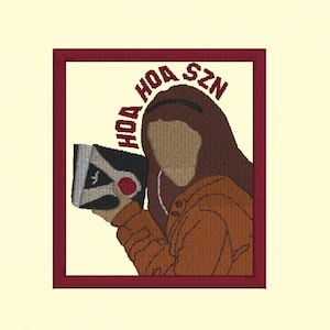 May include: Embroidered patch with a red border, featuring a cartoon illustration of a person wearing a brown hooded sweatshirt and orange jacket, holding a book with the text "HOA SZN" in a circle around the person's head.