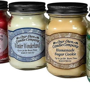 May include: Four glass jar candles with black lids. The candles are labelled "Our Own Candle Company" and have different scents: Mulled Cider, Winter Wonderland, Homemade Sugar Cookie, and Balsam Pine. Each candle has a burn time of up to 30 hours.