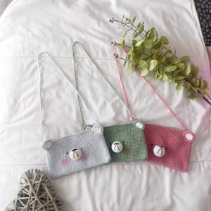 May include: Three crocheted bear-shaped purses with straps. The purses are light blue, green, and pink.