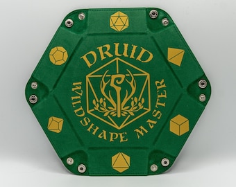 May include: A green, hexagonal dice rolling tray with gold lettering and symbols. The text reads "Druid Wildshape Master". The tray has metal snap closures at each point and is designed for tabletop gaming.