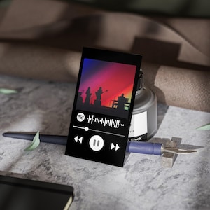 May include: A black card with a Spotify code and play controls. The card features a silhouette of a band performing on a stage with a colourful gradient background.
