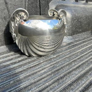 Puede incluir: Una cubitera de champ&aacute;n plateada con asas ornamentadas y un dise&ntilde;o con textura de concha. La cubitera tiene las palabras "CHAMPAGNE GOSSET" impresas en la parte delantera. La cubitera est&aacute; sobre una superficie texturizada.