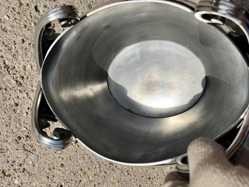Puede incluir: Un cuenco de metal plateado con asas decorativas. El cuenco tiene una abertura circular ancha y un interior liso y reflectante. Las asas presentan un dise&ntilde;o de volutas. El cuenco probablemente se utiliza para servir o exhibir.