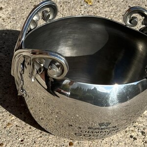 Puede incluir: Una cubitera de champ&aacute;n plateada con asas ornamentadas. La cubitera tiene forma redondeada y superficie reflectante, con las palabras "CHAMPAGNE GOSSET" visibles. Las asas presentan adornos de volutas.