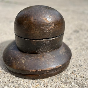 May include: A dark brown wooden hat form with a rounded top and a flat base. The form is made of two pieces that fit together.