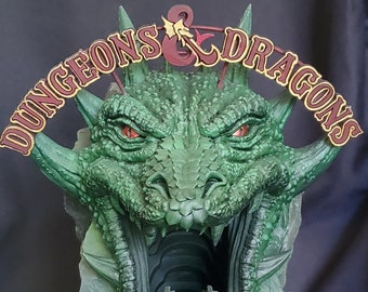 May include: A green dragon head sculpture with an open mouth, revealing a dark tunnel inside. The sculpture has a sign above it that reads "Dungeons & Dragons".