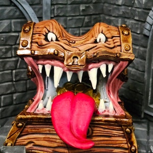 May include: A wooden treasure chest with a toothy, grinning face and a red tongue sticking out. The chest is painted brown with gold accents and has a brass lock.