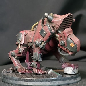 Könnte beinhalten: Eine rote und schwarze Robotertierfigur mit detailliertem Design. Die Figur ist in einer hockenden Position mit dem Kopf zur Seite gedreht. Die Figur steht auf einem schwarzen runden Sockel.